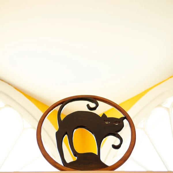 A wooden cutout of a black cat with an arched back, inside a circular frame.