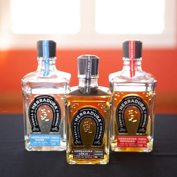 Three bottles of Herradura tequila, including Silver, Añejo, and Reposado, on a dark surface.