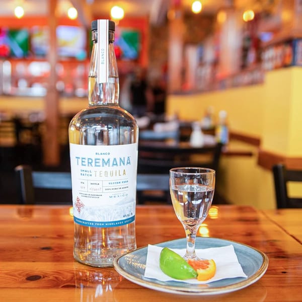 A bottle of Teremana Blanco tequila and a shot glass with lime and orange on a wooden table.
