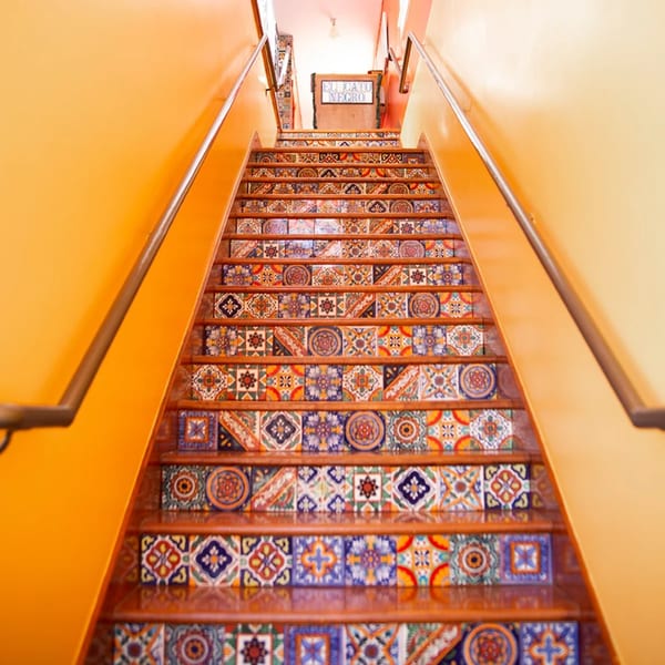 Staircase with colorful Mexican tile risers and orange walls leading to an "El Gato Negro" sign.