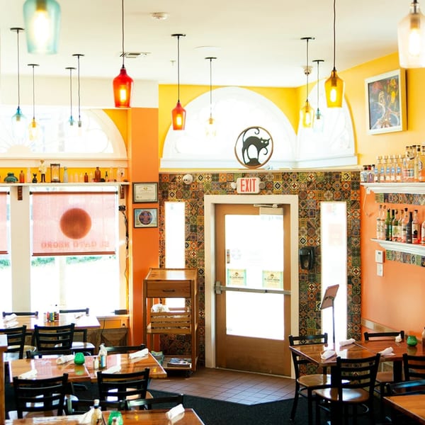 El Gato Negro's vibrant dining room with orange walls, colorful tile accents, and wooden tables.