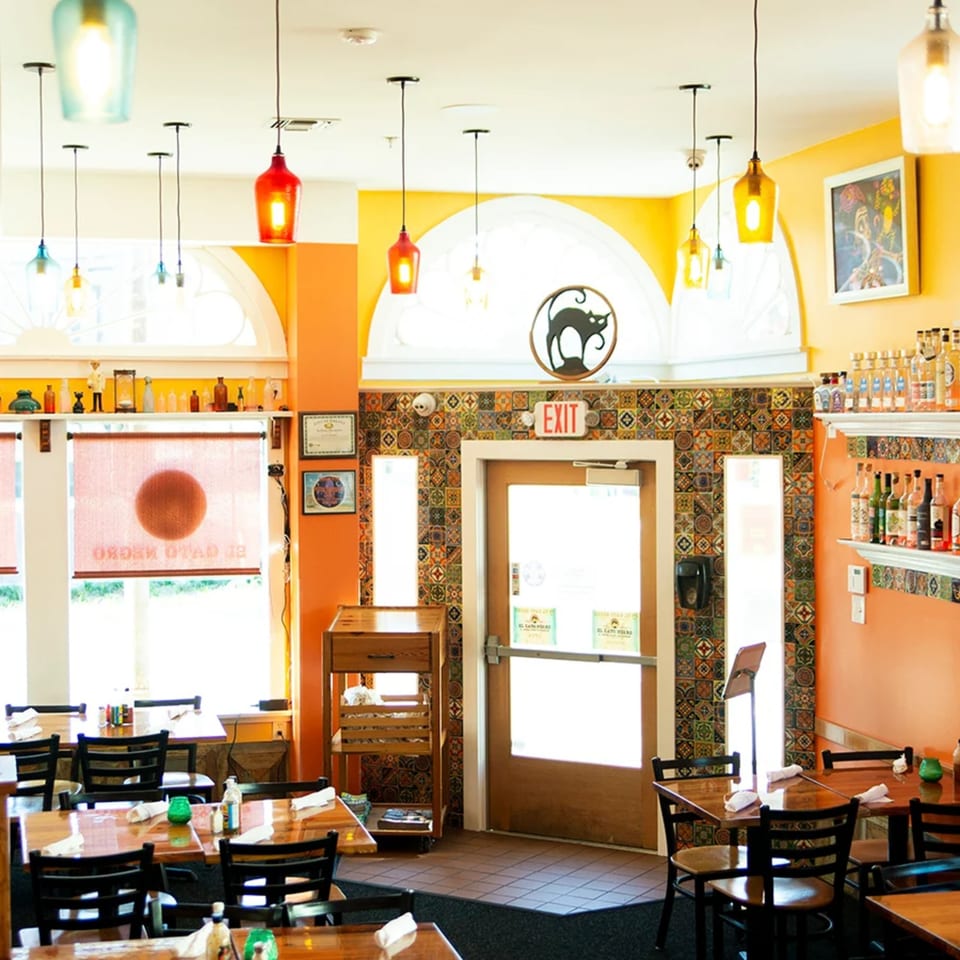 El Gato Negro's vibrant dining room with orange walls, colorful tile accents, and wooden tables.