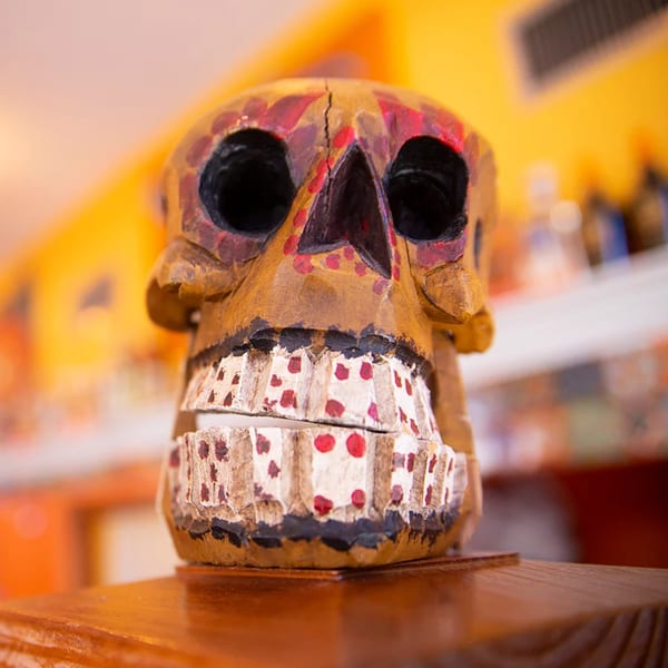 A colorful, hand-carved wooden skull, a traditional Mexican decoration, sits on a wooden surface.