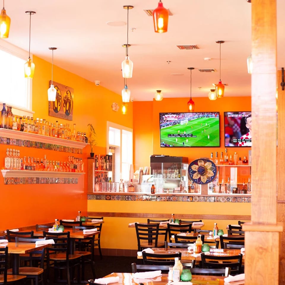 Vibrant orange walls, wooden tables, and a bar with liquor bottles and TVs showing soccer at El Gato Negro.