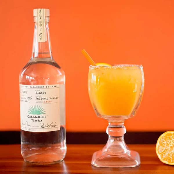 Casamigos Tequila bottle next to a vibrant orange margarita with a salted rim and orange slice.