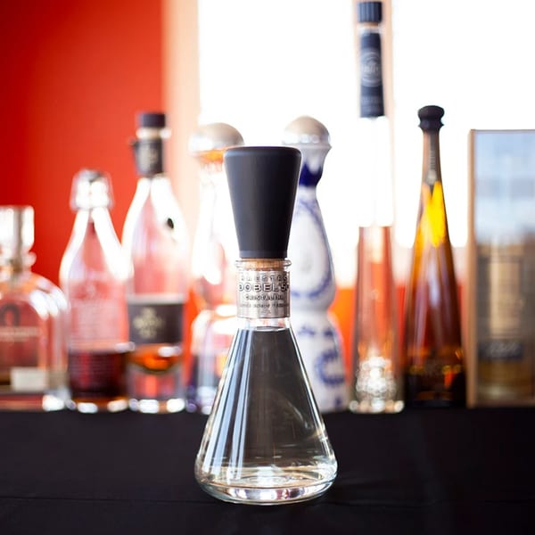 A clear bottle of Maestro Dobel 50 Cristalino tequila with other bottles blurred in the background.