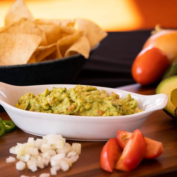 Fresh guacamole in a white dish, with tortilla chips, diced onions, tomatoes, and jalapeños.