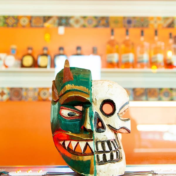 A green and white split mask, half demon, half skull, sits on a bar.