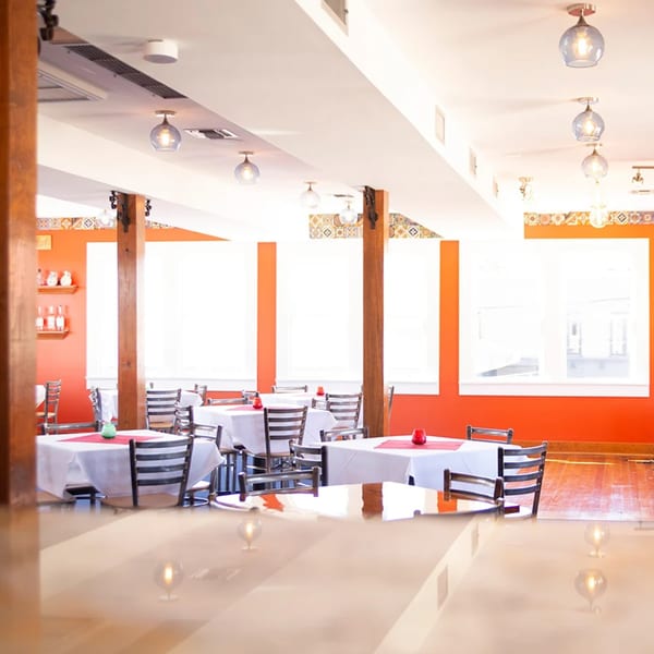 El Gato Negro dining room with orange walls, white tablecloths, and wooden chairs under blue glass pendant lights.