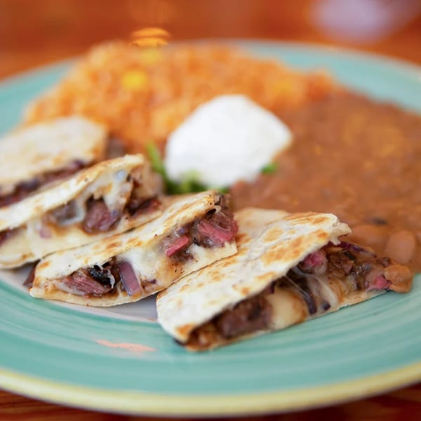 Steak quesadillas with melted cheese, served with refried beans, rice, and sour cream on a teal plate.