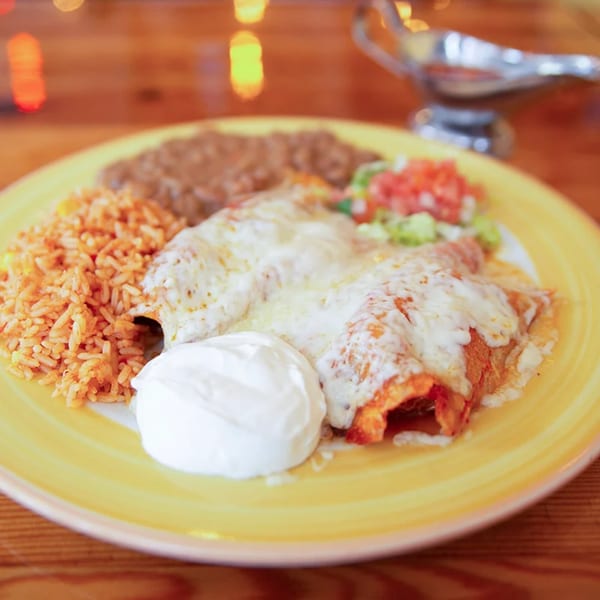 Two cheesy enchiladas with rice, refried beans, pico de gallo, and sour cream on a yellow plate.